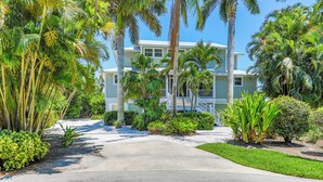 A two-story house with a front porch, surrounded by palm trees and well-maintained lawns.