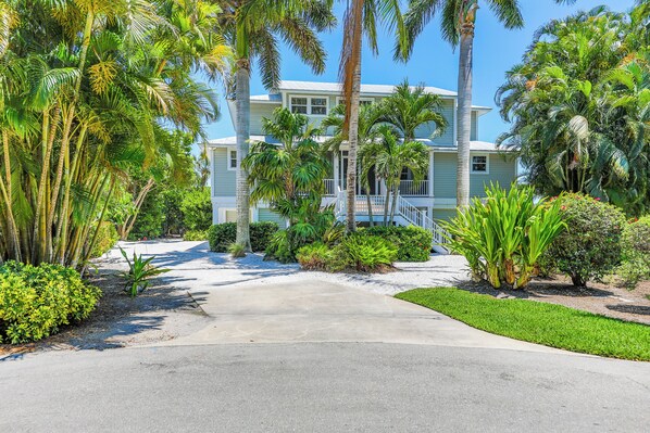 A two-story house with a front porch, surrounded by palm trees and well-maintained lawns.