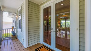 A covered porch with a wooden deck, a bird sculpture, and a glass door leading to an outdoor patio area.