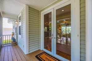 A covered porch with a wooden deck, a bird sculpture, and a glass door leading to an outdoor patio area.