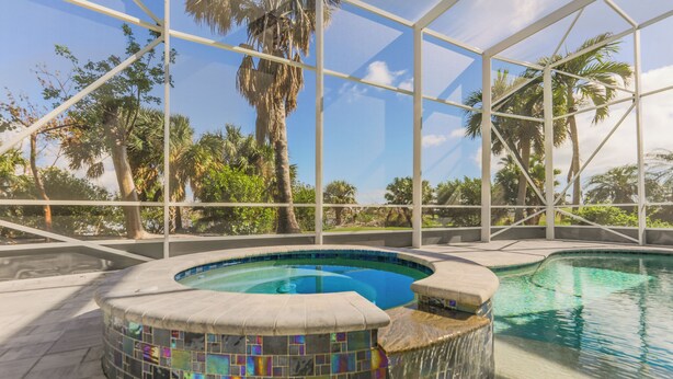 A swimming pool with a mosaic tile edge, surrounded by a glass enclosure, palm trees, and a clear sky.