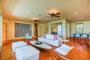 A spacious living room with a white sofa, a coffee table with flowers, a rocking chair, and a dining area with blue chairs and a table.