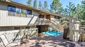 A wooden deck with a hot tub, a staircase, and a view of a forest.
