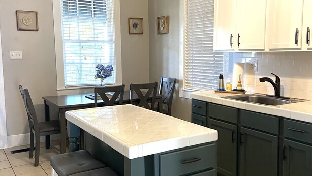 A kitchen with a central island, dark green cabinets, white countertops, and a ceiling fan. - Beautiful Benton Beauty (Saint Charles)