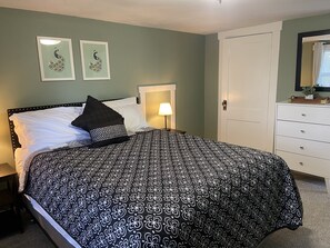 Ein ordentlich bezogenes Bett mit einem schwarz-weißen Bettdeckenmuster, einem weißen Kopfteil und zwei gerahmten Wandbildern darüber.
