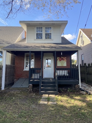 A two-story house with a front porch, a door, and a small garden area.