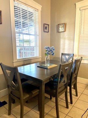 A dining area with a table and four chairs, a vase with flowers, and two framed pictures on the wall.
