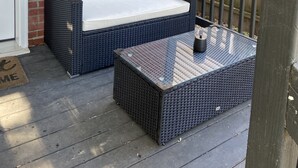 A covered porch with a wicker sofa and a glass-top table, a brick wall, and a wooden fence. - Beautiful Benton Beauty (Saint Charles)