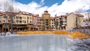 A multi-story hotel with a central courtyard featuring a frozen pond, surrounded by buildings with varied architectural styles. - Ultimate Location by InvitedHome | Hike, Bike, Shops, Restaurants, Gondola (Mountain Village)
