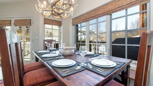 A dining area with a wooden table set for four, a chandelier, and large windows with views of the outdoors. - Ultimate Location by InvitedHome | Hike, Bike, Shops, Restaurants, Gondola (Mountain Village)