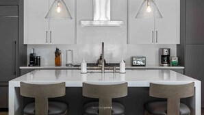 Une cuisine moderne dotée d’un îlot central, d’appareils électroménagers en acier inoxydable et de luminaires suspendus.