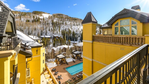 Un bâtiment jaune doté d’une piscine, d’un espace extérieur aménagé et offrant une vue sur des montagnes enneigées.
