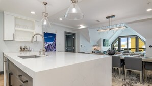 Une cuisine moderne dotée d’un grand îlot central, de luminaires suspendus et d’un coin repas avec un plafond haut et une verrière.