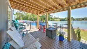 A covered deck with Adirondack chairs, a pool table, and a view of a lake.