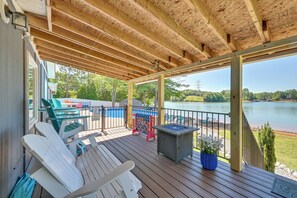 Una terraza cubierta con sillas Adirondack, mesa de billar y vista a un lago.