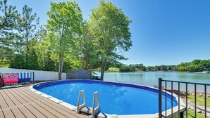 A swimming pool on a wooden deck with a view of a lake and trees.