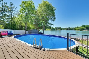 Piscina en una terraza de madera con vista a un lago y árboles.