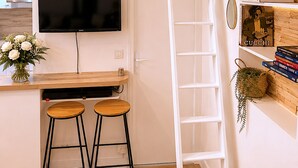 A modern kitchen with a built-in TV, wooden bar stools, a ladder, and a bookshelf with books and decorative items.