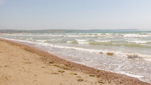A beach with waves, pebbles, and distant hills.