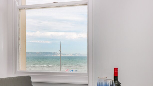 A room with a view of the sea, a table with a bottle and glasses, and a chair.
