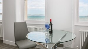 A modern room with a glass table, a grey chair, and a view of the sea through large windows.