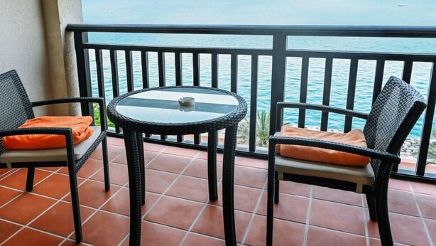 Un balcon avec deux fauteuils en osier et une table en verre, donnant sur une étendue d’eau.