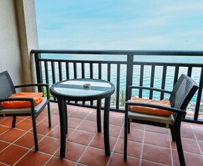 Ein Balkon mit zwei Korbstühlen und einem Glastisch, mit Blick auf ein Gewässer.