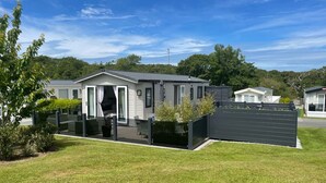 En moderne mobilbolig med en overdækket terrasse, stor skydedør og en have afgrænset af et hegn.