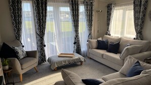 En stue med en beige sofa, et lille rundt bord og en gulvlampe.