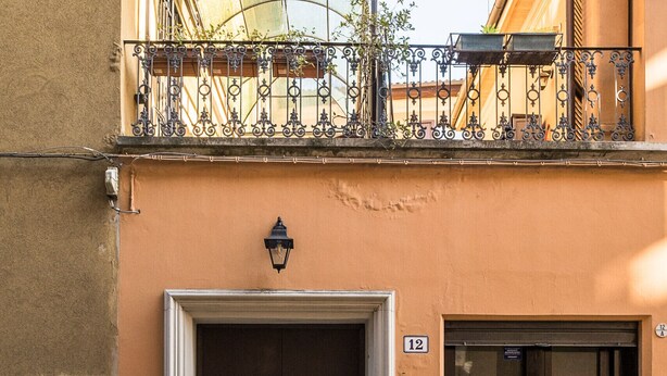 Ein Gebäude mit einer großen schwarzen Tür, einem Balkon mit Metallgeländern und einem kleinen Fenster mit einem Metallgitter.
