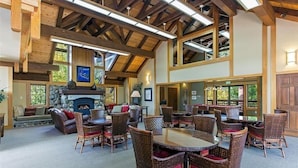 A spacious indoor area with a fireplace, multiple wicker tables and chairs, and large windows allowing natural light.