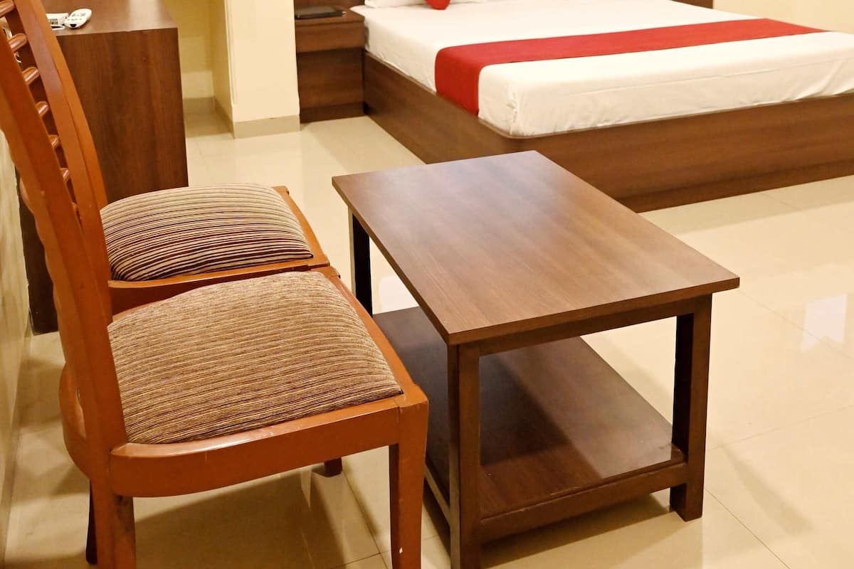 Quarto de hotel com uma cama, uma cadeira de madeira, uma mesinha, um guarda-roupa e um ventilador de teto.