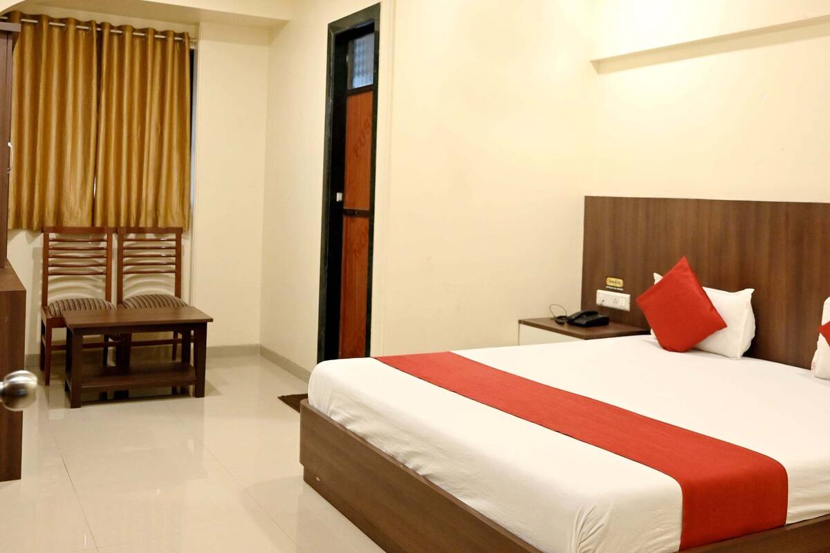 Quarto de hotel com uma cama grande, uma mesa de cabeceira de madeira, uma escrivaninha com cadeira e um ventilador de teto.