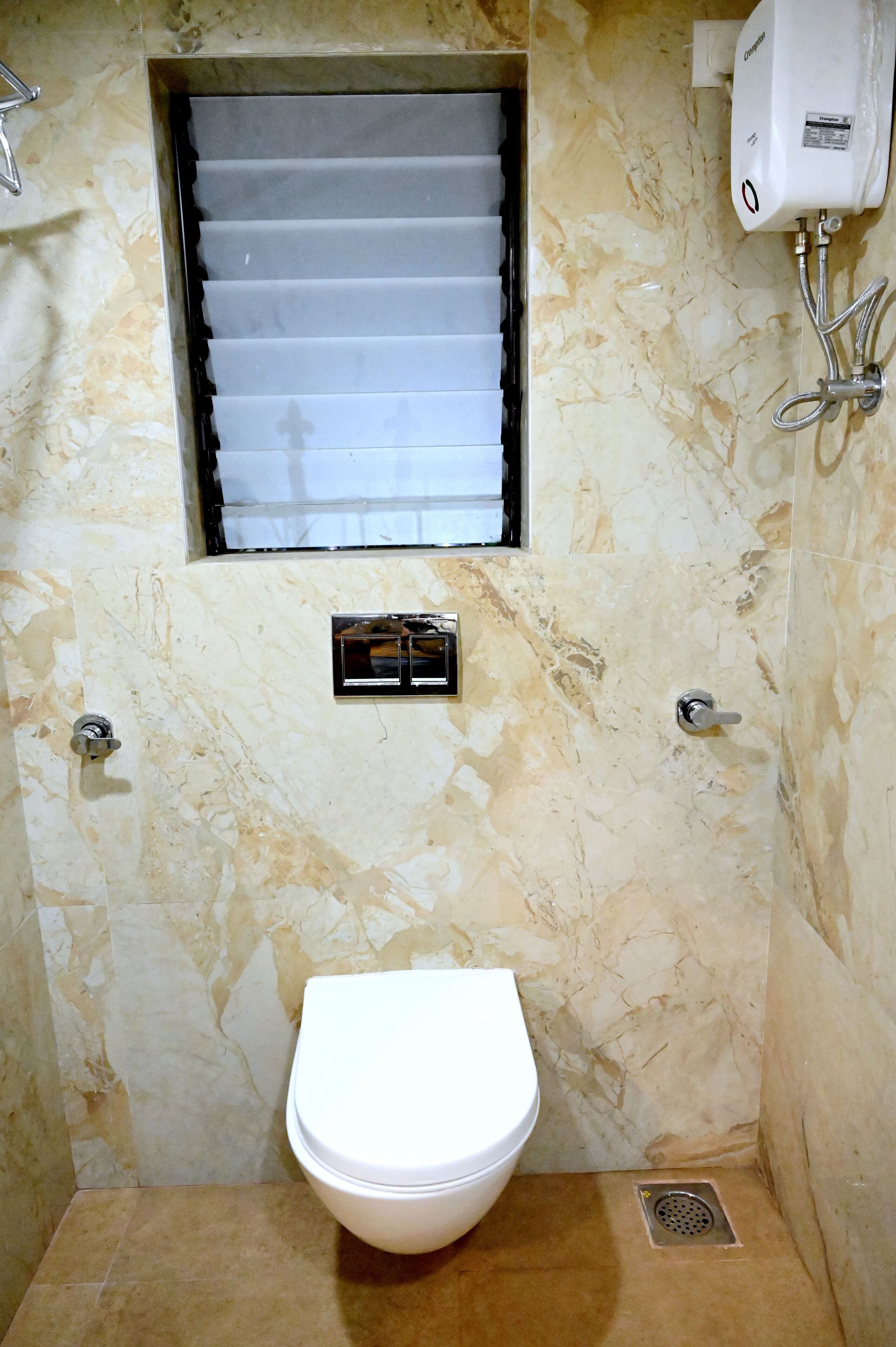 Un baño con inodoro, ventana con persianas, calentador de agua y desagüe de ducha.