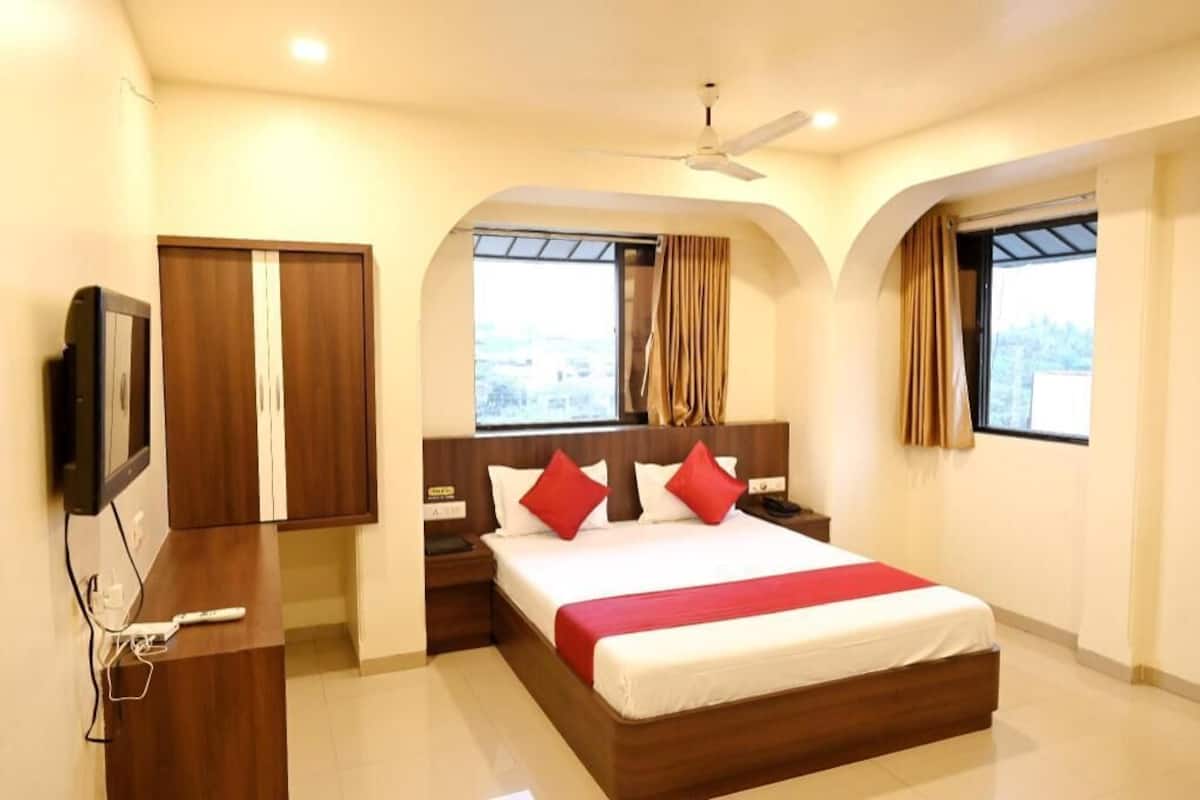 Quarto de hotel com cama, televisão, escrivaninha e janela com cortinas.