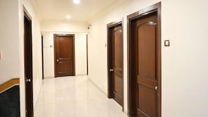 Un pasillo con tres puertas de madera, paredes blancas y suelo de baldosas.