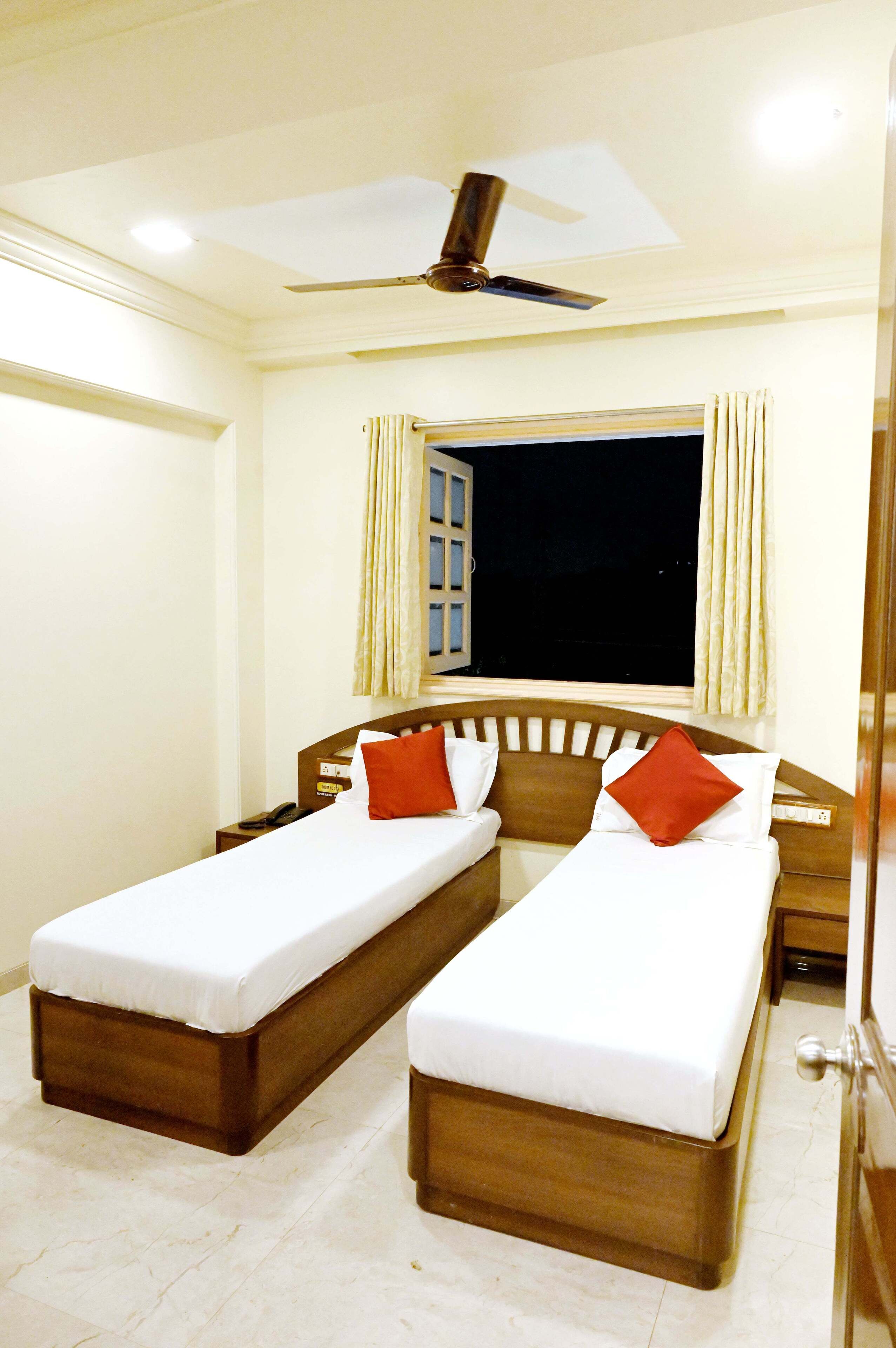 A hotel room with two single beds, a ceiling fan, a window with curtains, and a night view outside.
