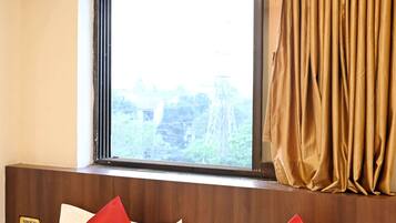 Habitación de hotel con una cama, dos almohadas rojas, un ventanal con vistas a zonas verdes y una cortina.