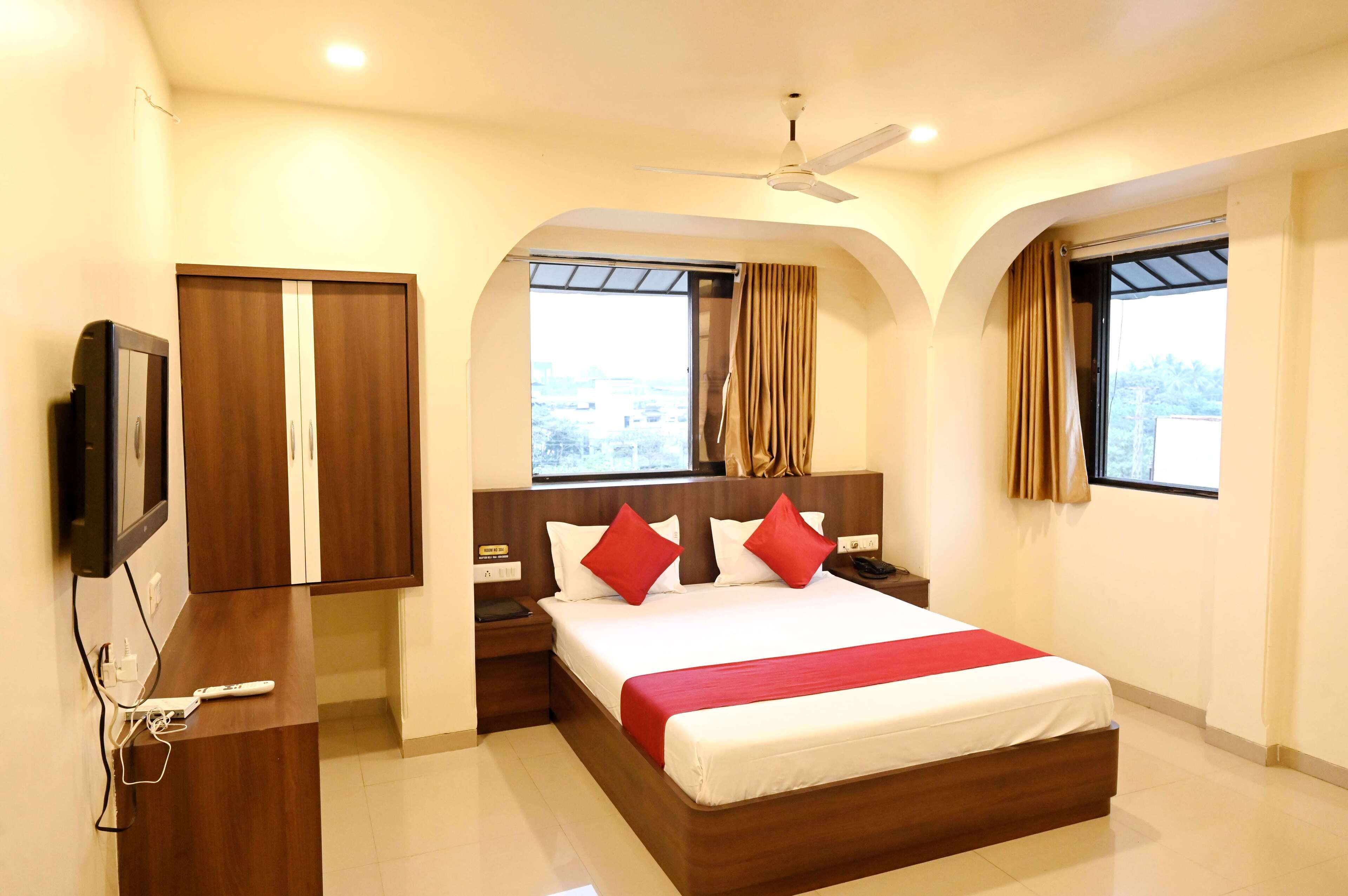 A hotel room with a bed, a TV, a wardrobe, and a window with curtains.