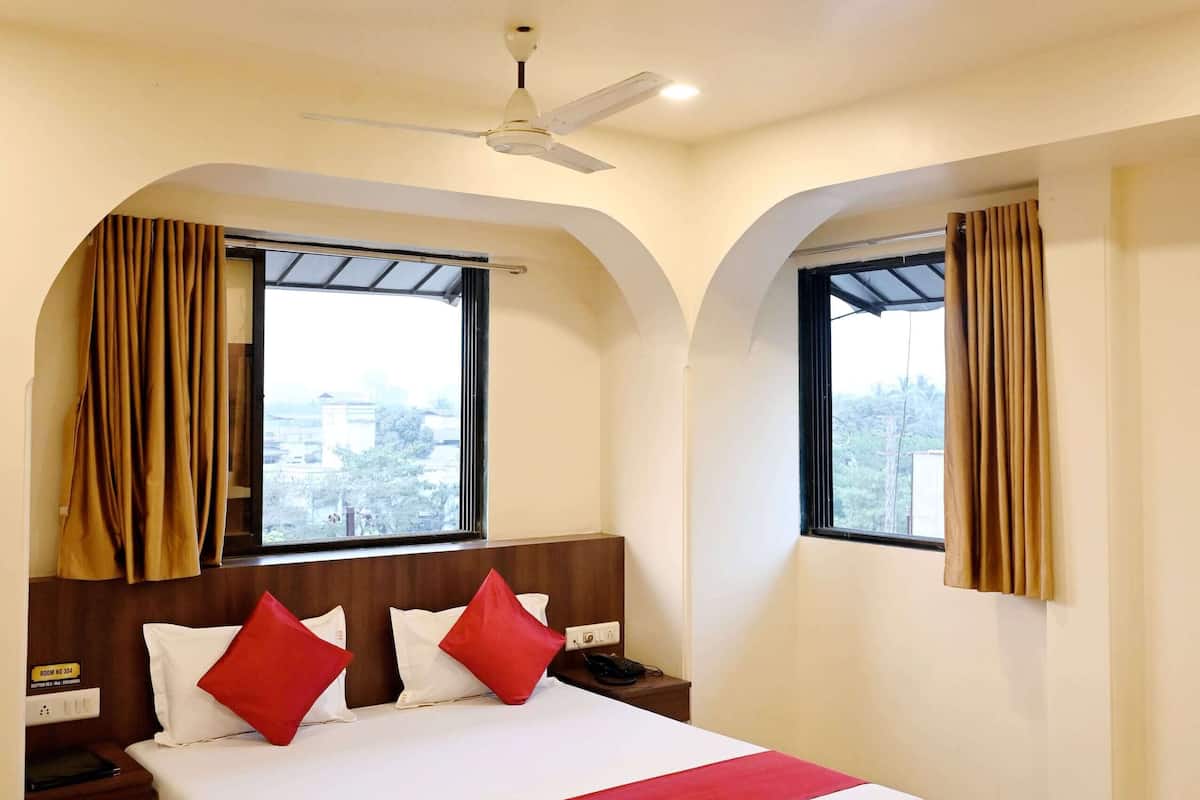 Quarto de hotel com cama, duas janelas com cortinas, ventilador de teto e vista para o exterior.
