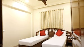 Una habitación de hotel con dos camas individuales, un ventilador de techo y una ventana con cortinas.