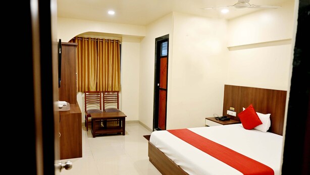 Une chambre d’hôtel comprenant un lit, un bureau, une chaise, une armoire et une fenêtre avec des rideaux.