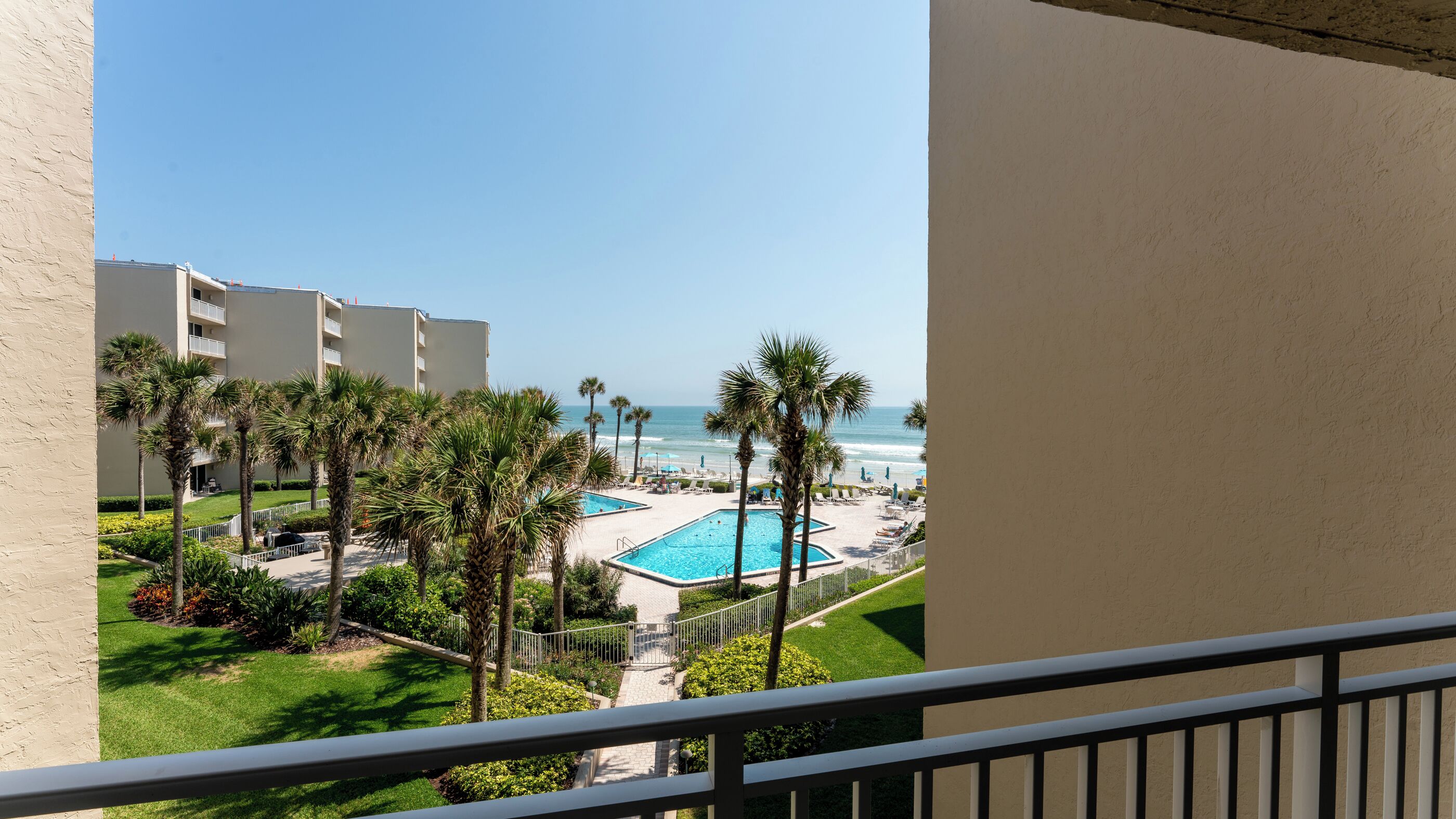 A pool area with a view of the ocean, surrounded by palm trees and a building.