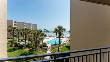 A pool area with a view of the ocean, surrounded by palm trees and a building.