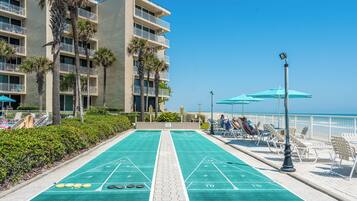 Un terrain de jeu de shuffleboard offrant une vue sur un hôtel en bord de mer et des palmiers.