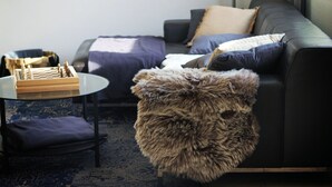 A modern living room with a leather sofa, a glass coffee table, a fur ottoman, and a chessboard.