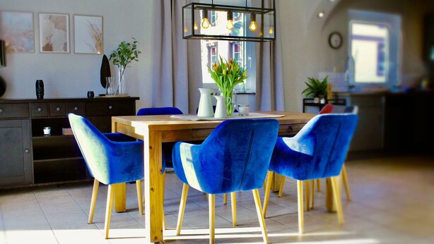 A dining area with a wooden table and blue chairs, a vase with flowers, and a modern pendant light.