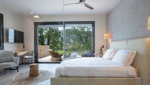 A modern bedroom with a large bed, a desk, and a chair, featuring a view of the outdoors through a glass door. - High-end Villa Lyra close to Desimi beach with heated pool (Lefkada)