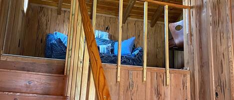 A wooden staircase with a handrail leading to a bedroom with a bed and a window.