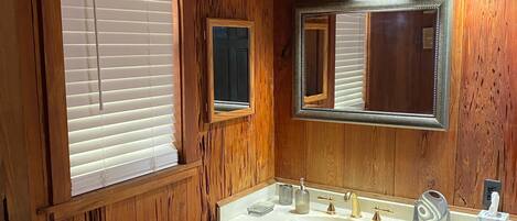 A wooden bathroom with a sink, mirror, and window with blinds.